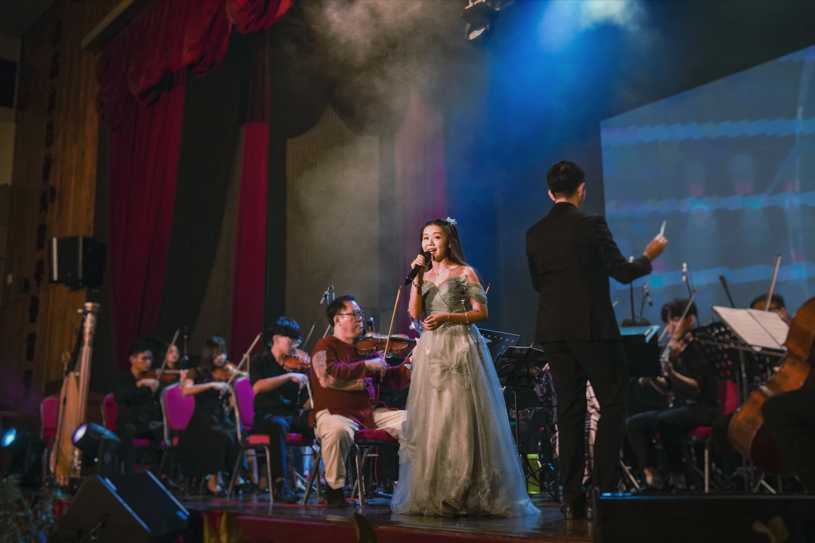 Eugenie singing in a silver gown alongside the orchestra and conductor