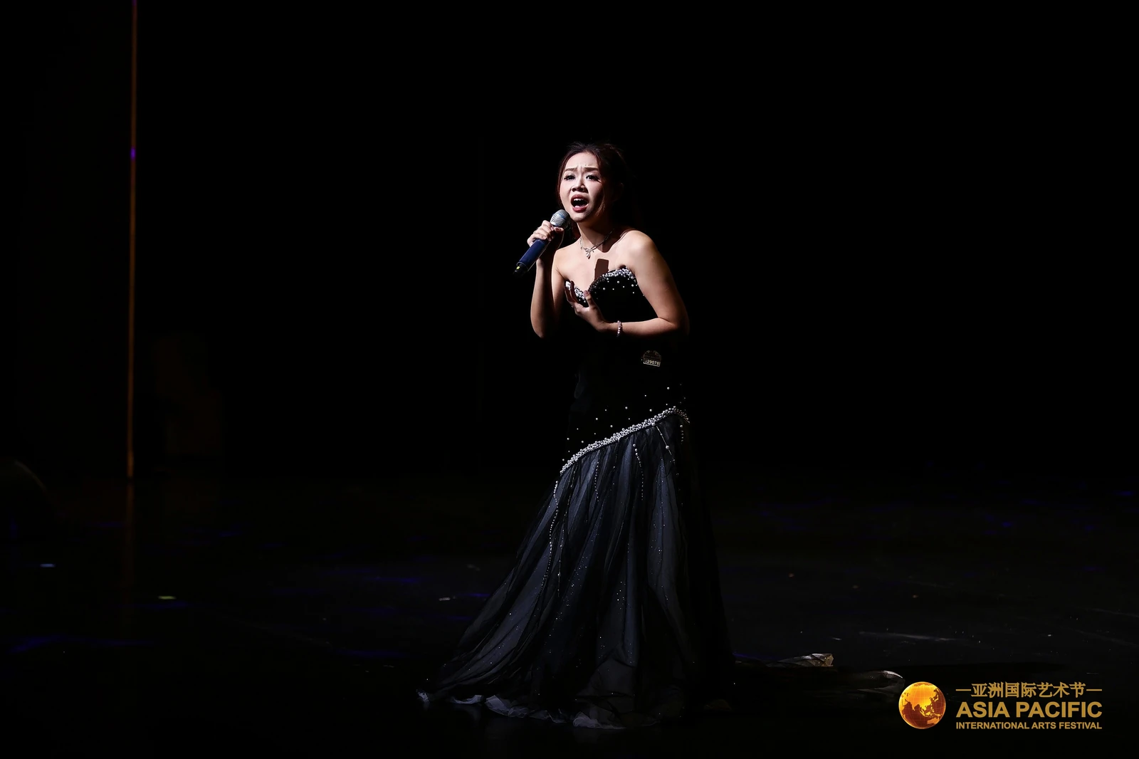 Eugenie singing in a black evening gown on a dark stage at the Asia Pacific International Arts Festival