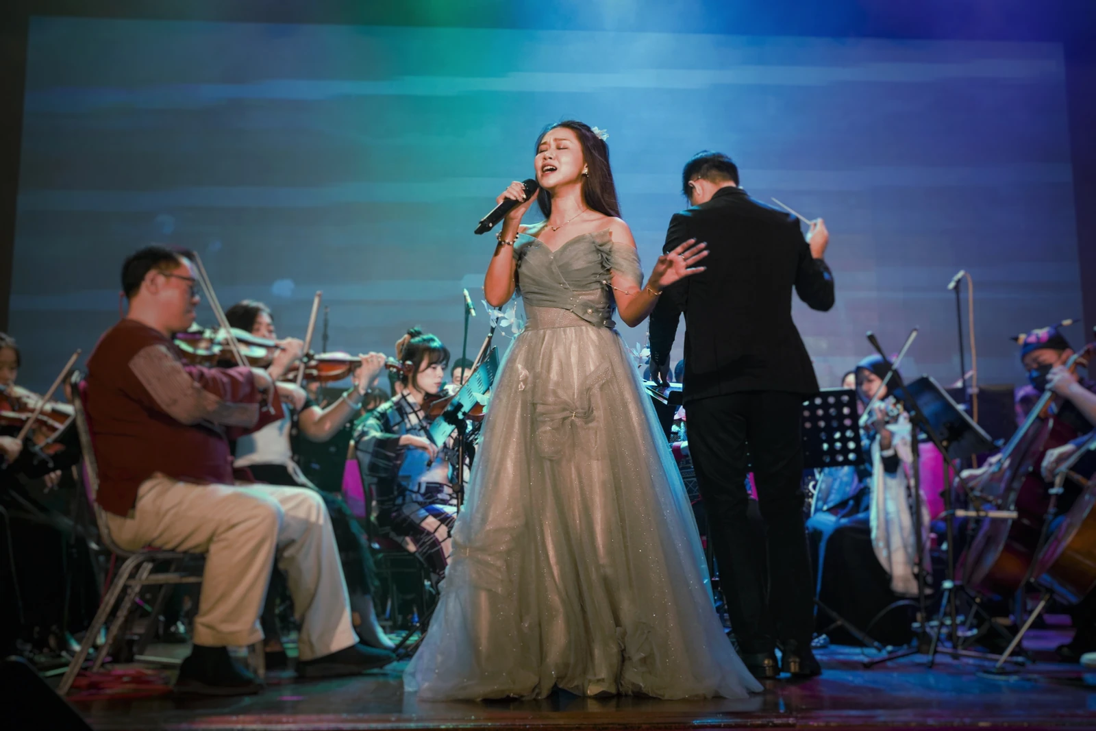 Eugenie singing with her eyes closed and one hand outstretched, surrounded by orchestral musicians